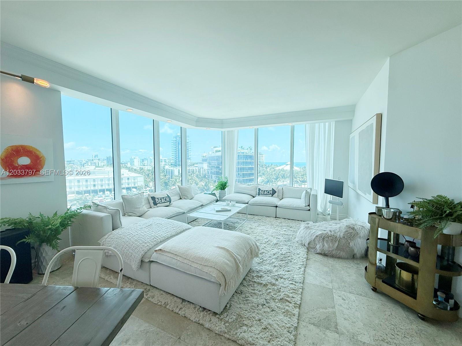 A bright living room features a large white sectional sofa, a textured rug, and floor-to-ceiling windows — 300 S Pointe Dr # 705, Miami Beach FL 33139, MIAMI BEACH, FL
