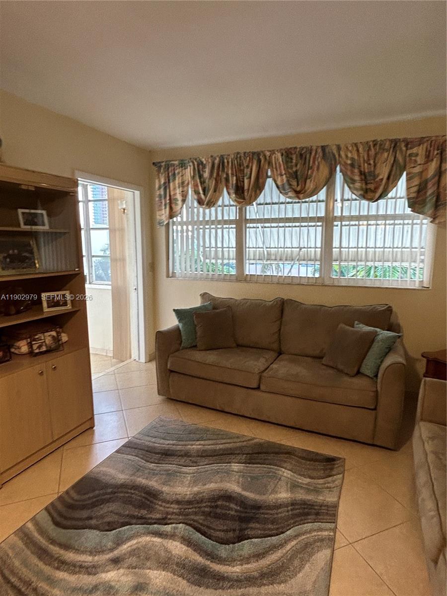 A living room features a beige sofa, a patterned area rug, and tile flooring — 1333 E Hallandale Beach Blvd # 406, Hallandale Beach FL 33009, HALLANDALE BEACH, FL