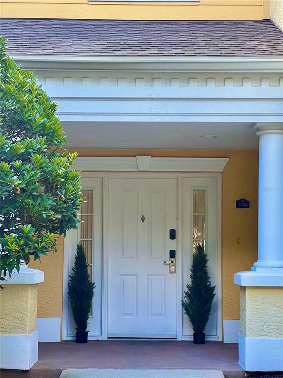 A white front door with sidelights is framed by two potted evergreen trees and columns — 1304 SEVEN EAGLES COURT UNIT 1304, REUNION, FL