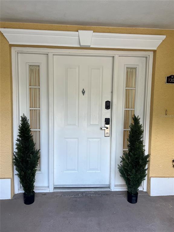 A white front door with sidelights and two potted evergreen trees on a porch — 1304 SEVEN EAGLES COURT UNIT 1304, REUNION, FL