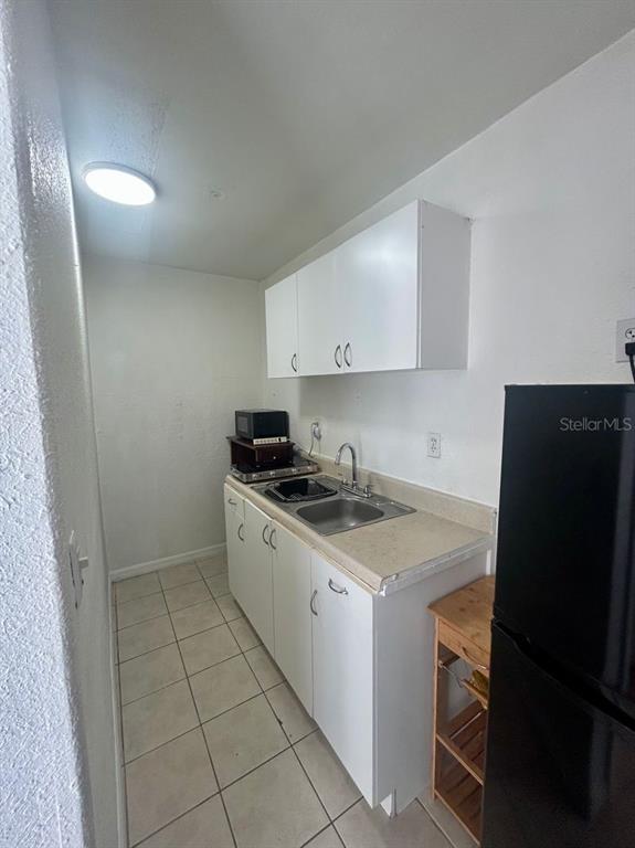 A small kitchen features white cabinets, a stainless steel sink, and light-colored tile flooring — 7302 WOODHALL COURT, TAMPA, FL