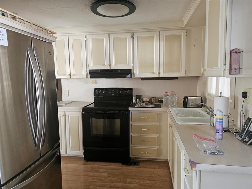 A kitchen features white cabinets with beige panels, a black stove, and stainless steel refrigerator — 104 IXORA WAY, LEESBURG, FL