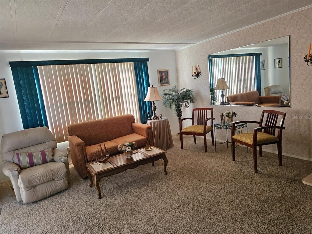 A living room features a sofa, two wooden chairs, a recliner, and a large wall mirror — 104 IXORA WAY, LEESBURG, FL