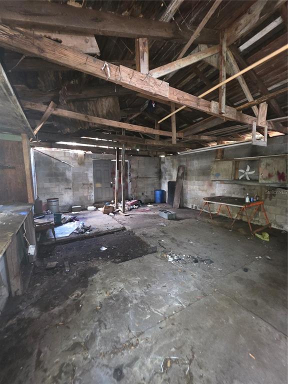 An interior view of a dilapidated, unfinished garage with exposed wooden rafters and concrete walls — 215 10TH WAHNETA STREET W, WINTER HAVEN, FL