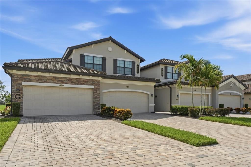 A two-story suburban house with a stone facade, multiple garage doors, and a paved driveway — 6055 WORSHAM LANE UNIT 101, BRADENTON, FL