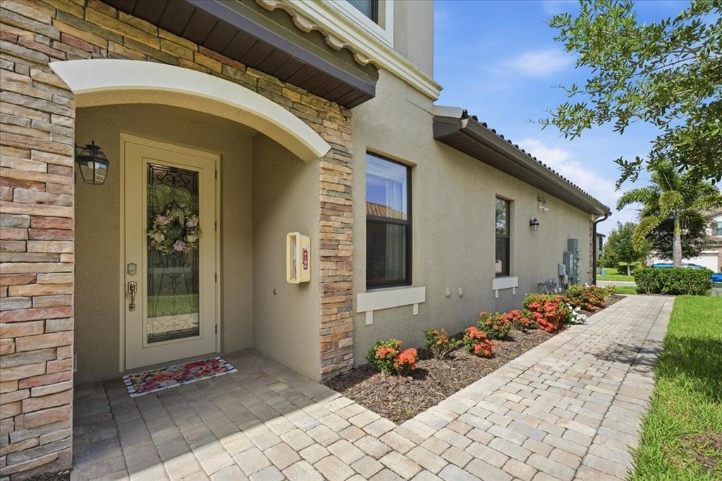 A stone-accented house entrance features a glass-paneled front door, a paved walkway, and landscaping — 6055 WORSHAM LANE UNIT 101, BRADENTON, FL