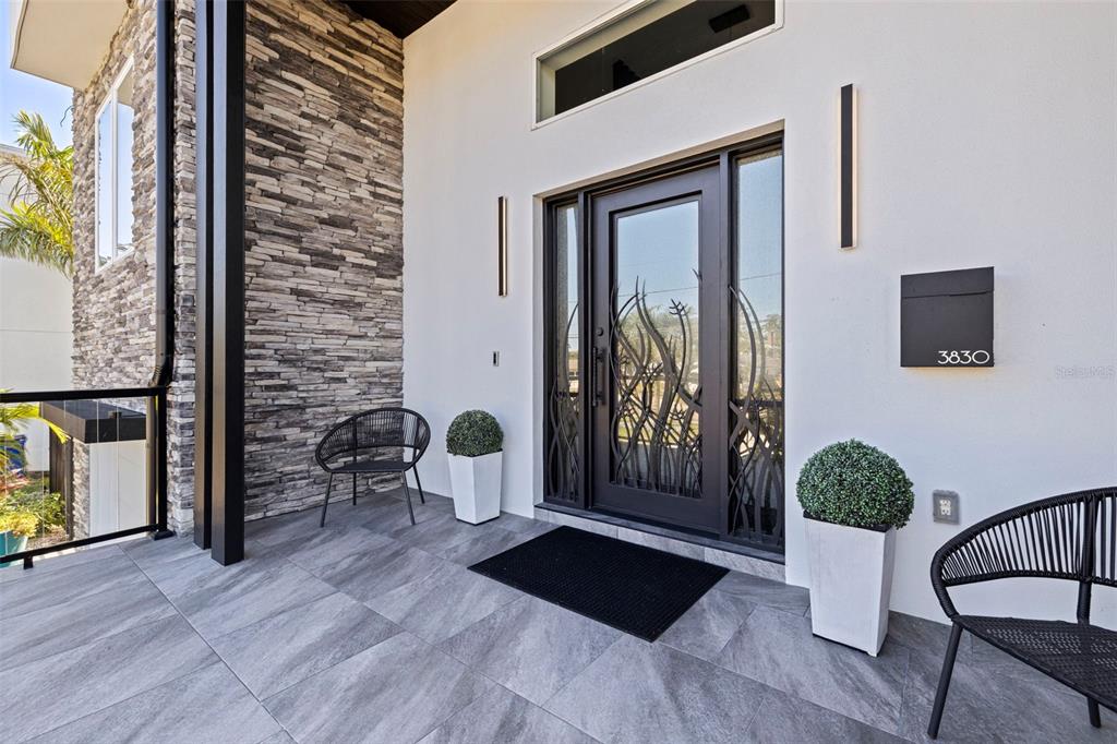 A modern entryway features a decorative glass door, stone siding, and two black patio chairs — 3830 SHORE ACRES BOULEVARD NE, ST PETERSBURG, FL