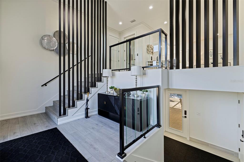 A modern entryway features a staircase with black vertical slats and a glass railing — 3830 SHORE ACRES BOULEVARD NE, ST PETERSBURG, FL