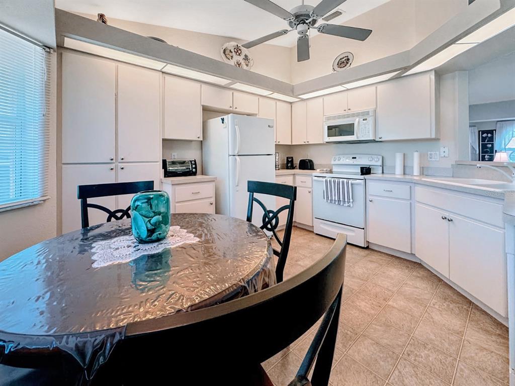 A kitchen features white cabinets, white appliances, a ceiling fan, and a round dining table — 18353 GRACE AVENUE, PORT CHARLOTTE, FL
