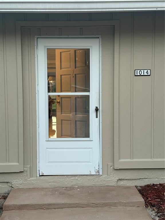 A white storm door with a glass panel is mounted on a beige exterior wall — 1014 VILLA LANE UNIT 7, APOPKA, FL
