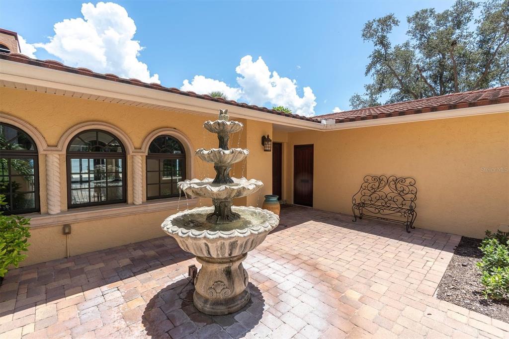 A stone tiered fountain sits in the center of a paved courtyard with stucco walls — 5810 BAHAMA SHORES DRIVE S, ST PETERSBURG, FL