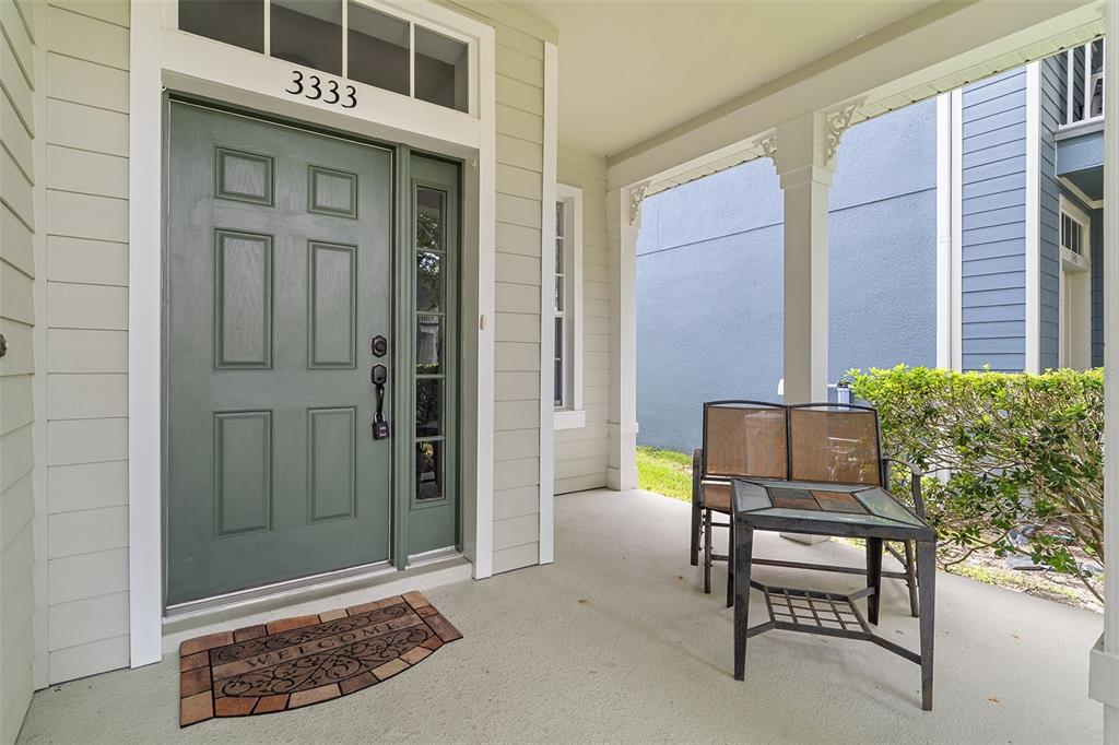 A covered front porch features a sage green door, a welcome mat, and patio furniture — 3333 BRACKEN FERN DR, ST CLOUD, FL