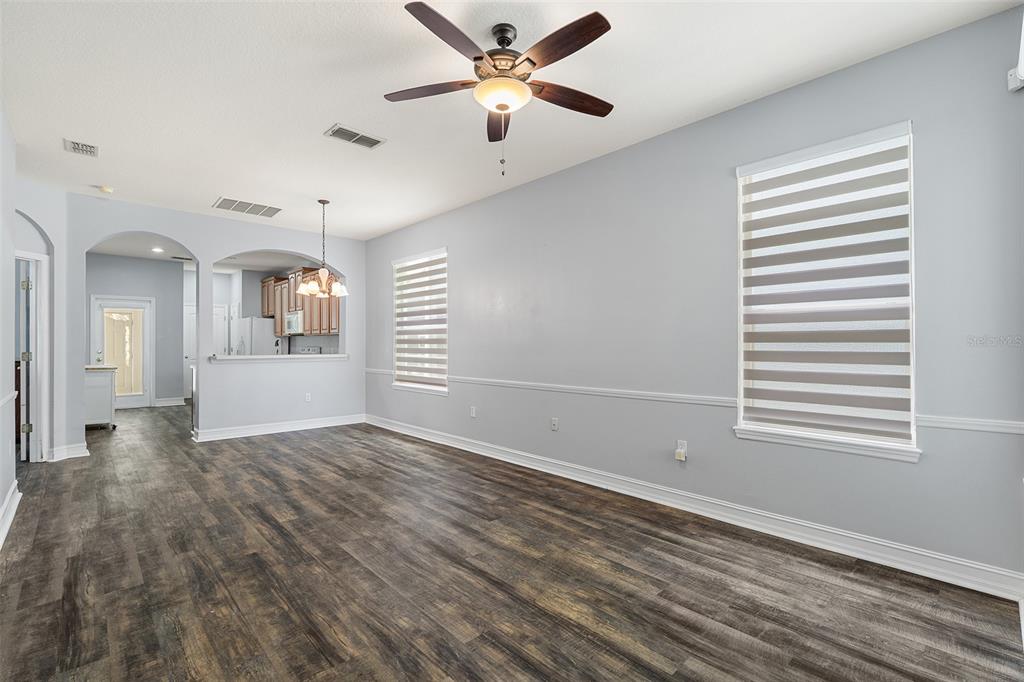 An empty living room features light gray walls, wood-look flooring, a ceiling fan, and windows — 3333 BRACKEN FERN DR, ST CLOUD, FL
