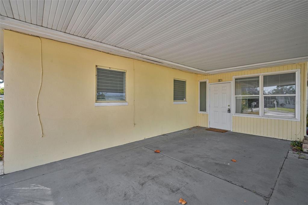 A covered concrete carport leads to a white front door and adjacent windows — 2476 CORONADO WAY, DUNEDIN, FL