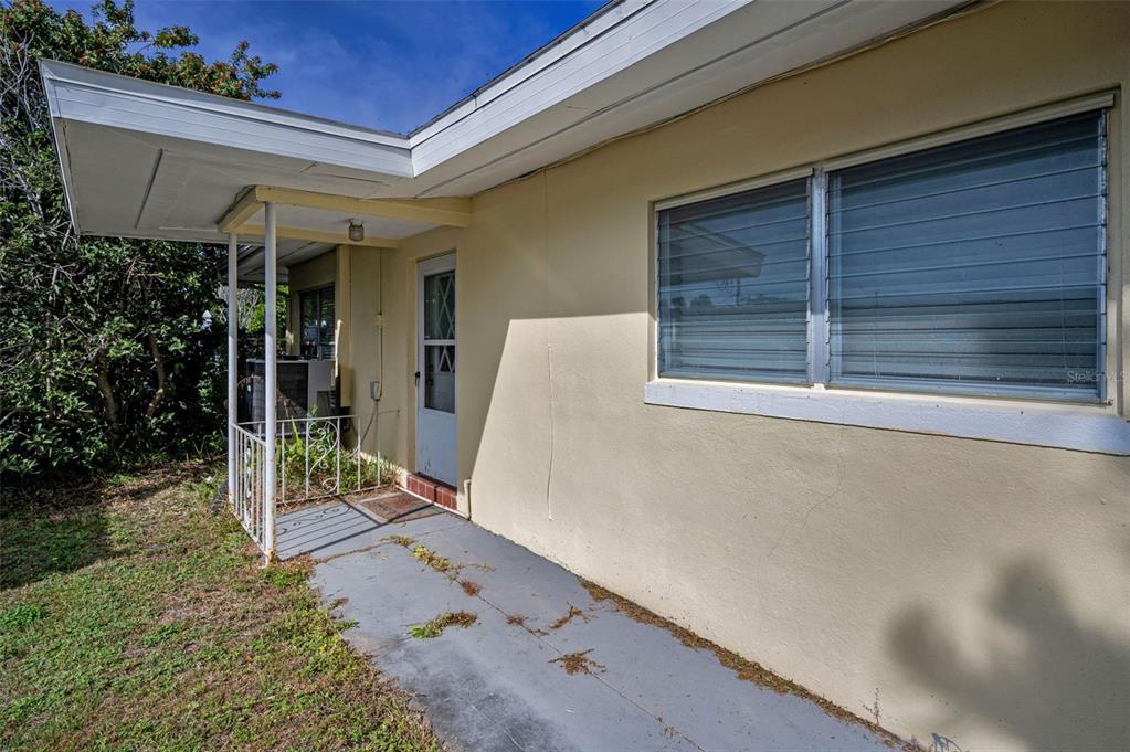 A side view of a house exterior featuring a concrete patio, metal railing, and jalousie windows — 2476 CORONADO WAY, DUNEDIN, FL