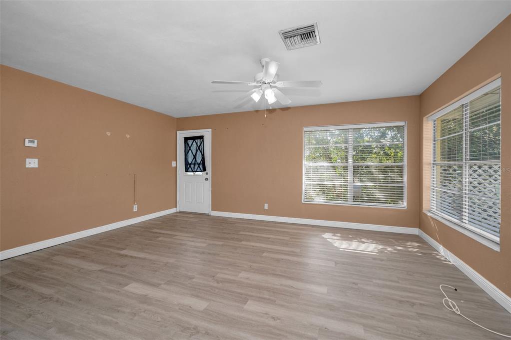 An empty living room with tan walls, light wood-look flooring, a ceiling fan, and windows — 2476 CORONADO WAY, DUNEDIN, FL
