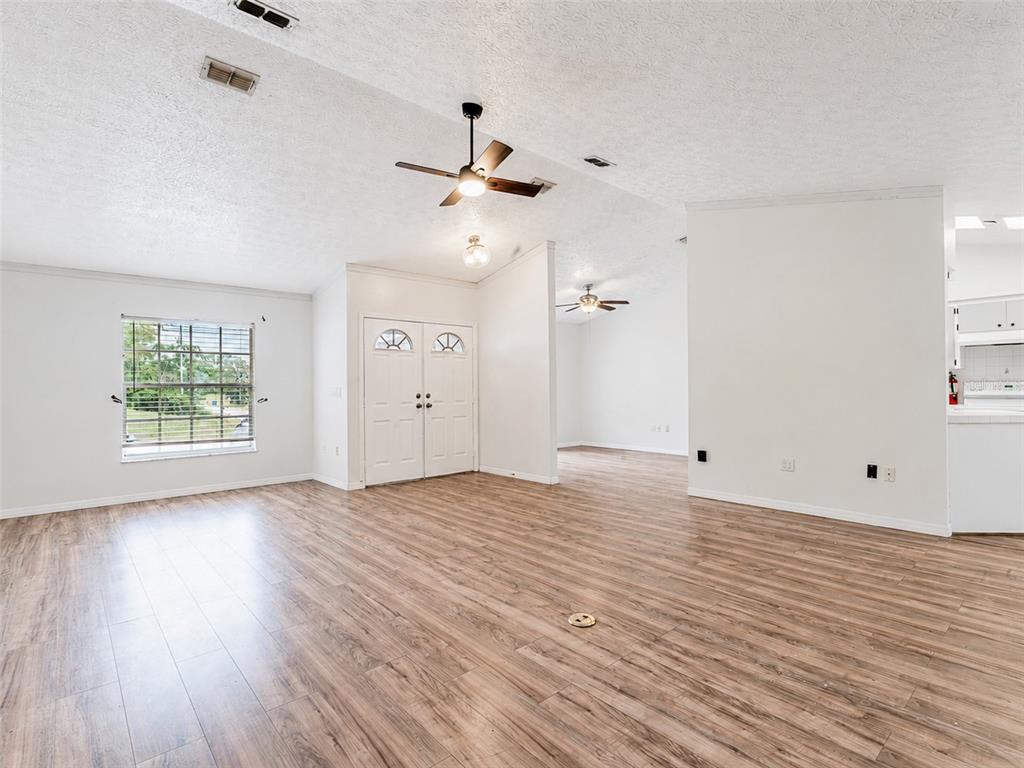 An open-concept living area features wood-look flooring, white walls, ceiling fans, and double doors — 265 CLEARFIELD AVENUE, SPRING HILL, FL