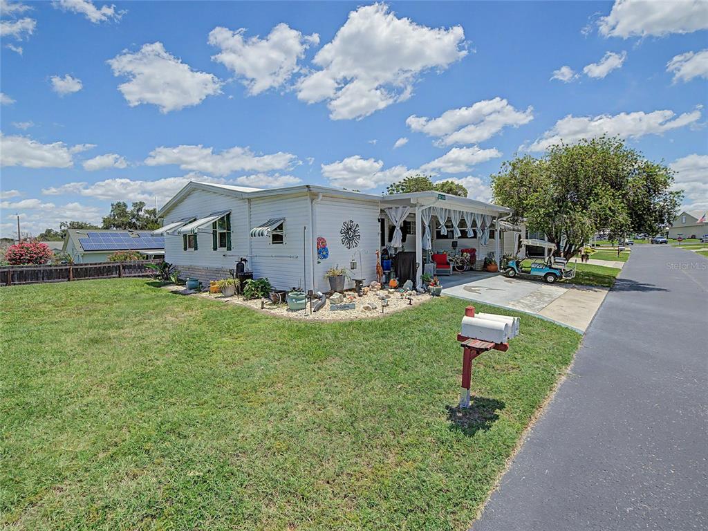 A single-story mobile home with a carport, a golf cart, and a grassy yard — 37513 CAMPO AVENUE, ZEPHYRHILLS, FL