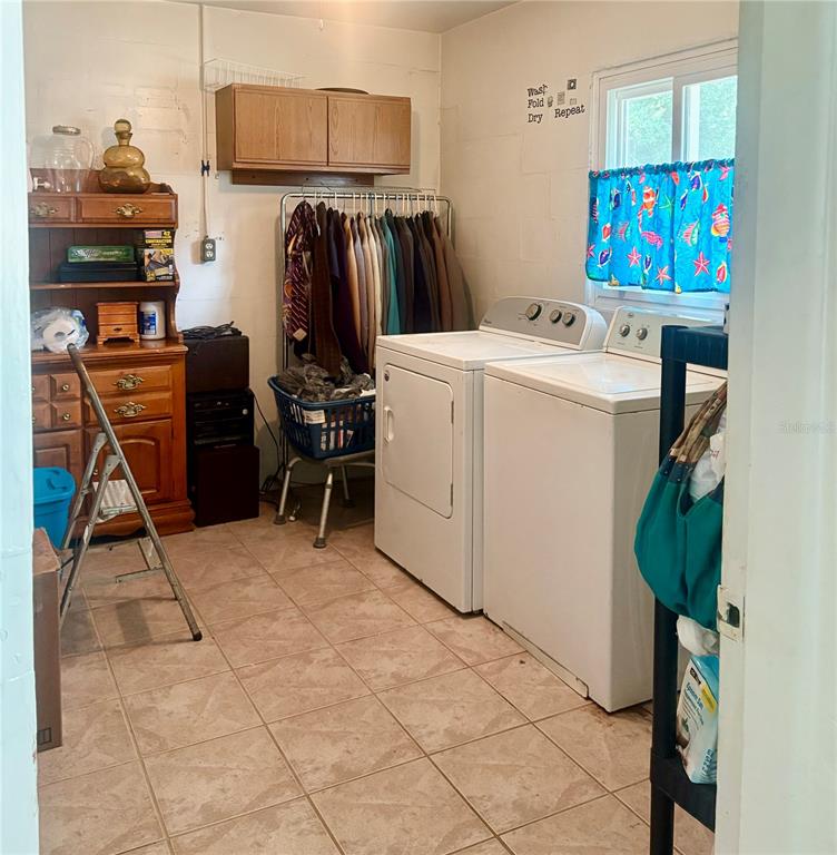 A laundry room features a washer, dryer, clothing rack, wooden hutch, and tile flooring — 107 E PALM STREET, DAVENPORT, FL