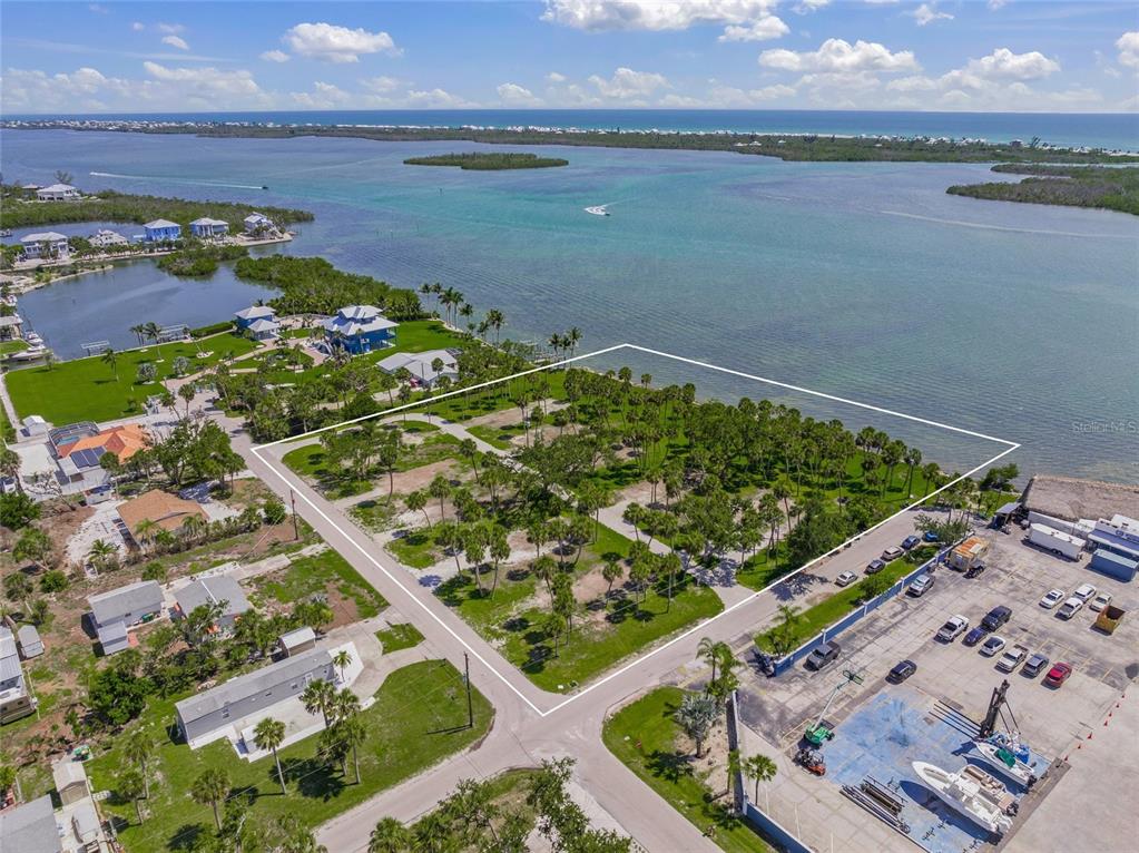 An aerial view shows a vacant, palm-dotted waterfront lot outlined in white near a marina — 1 RASCHE ROAD, ENGLEWOOD, FL