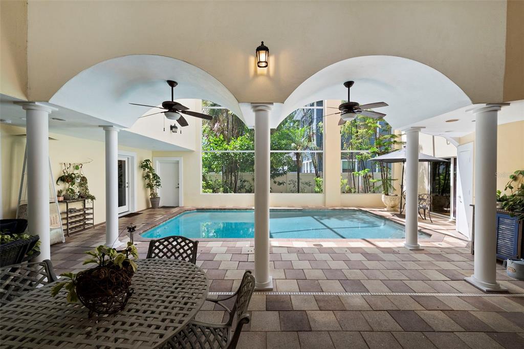 A covered patio with a swimming pool, columns, and ceiling fans overlooks a screened-in yard — 4106 W SAN MIGUEL STREET, TAMPA, FL