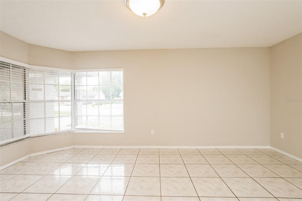 An empty room with beige walls, light-colored tile flooring, and a bay window — 2680 SWEET SPRINGS STREET, DELTONA, FL