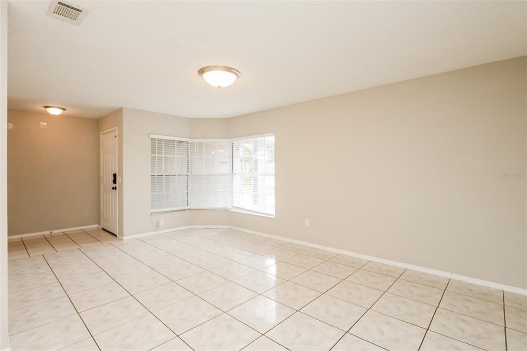 An empty room with beige walls, light-colored tile flooring, and a bay window — 2680 SWEET SPRINGS STREET, DELTONA, FL