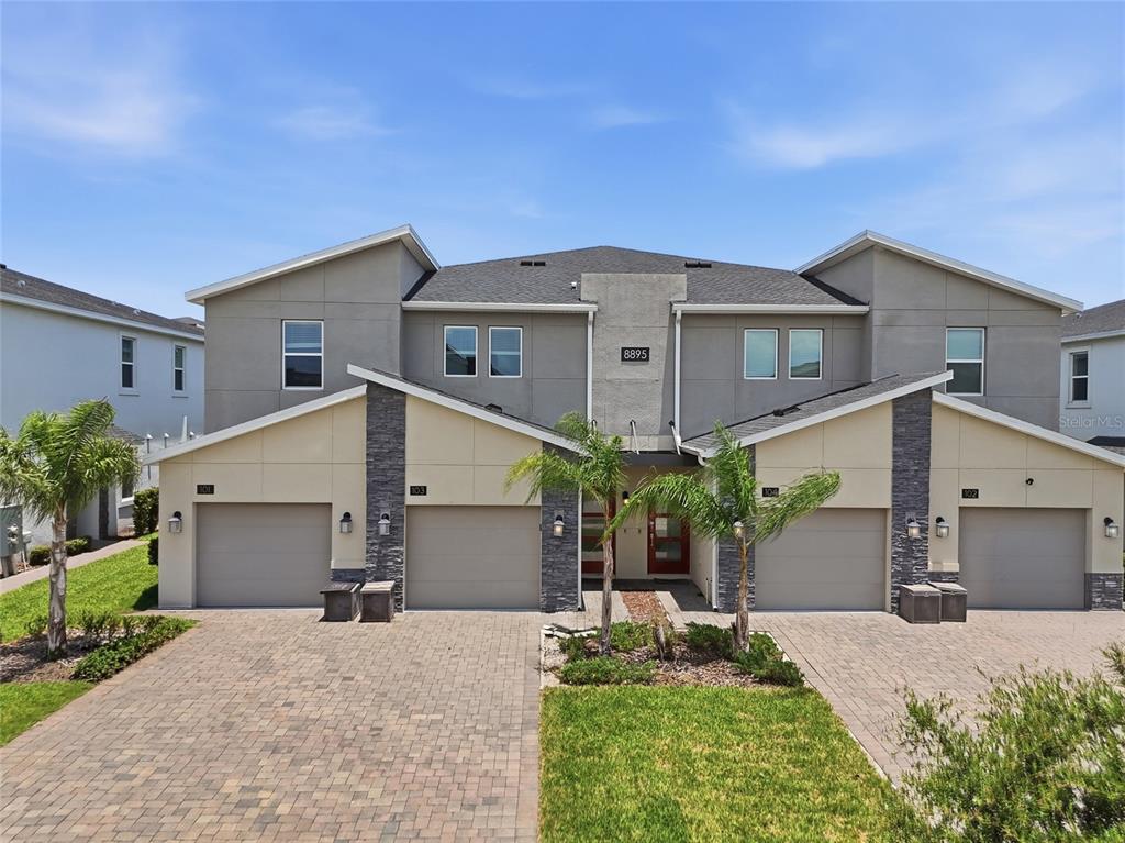 A two-story multi-family building features four garage doors, stone accents, and a paved driveway — 8895 CABOT CLIFFS DRIVE UNIT 103, DAVENPORT, FL