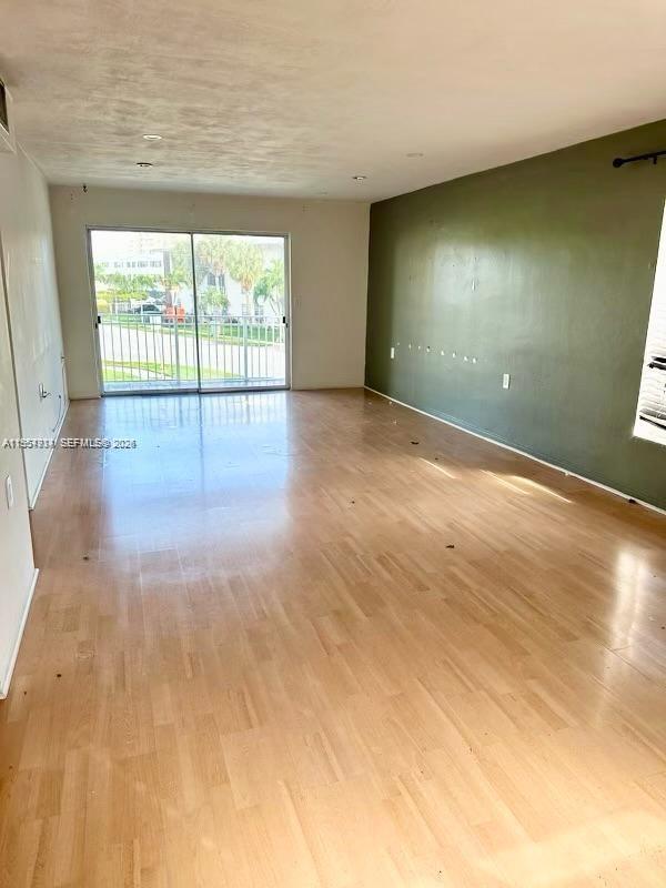 An empty living room features light wood flooring, an olive green wall, and sliding glass doors — 1631 NE 114th St # 201, Miami FL 33181, MIAMI, FL