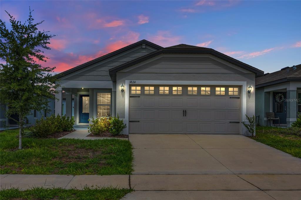 A single-story house with a two-car garage and a front porch at sunset — 3824 CORSICAN PLACE, LAKE ALFRED, FL