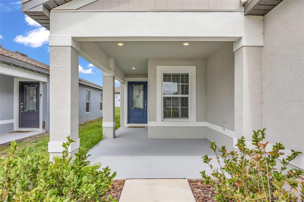 A covered front porch features a blue door, a window, and concrete flooring — 3824 CORSICAN PLACE, LAKE ALFRED, FL