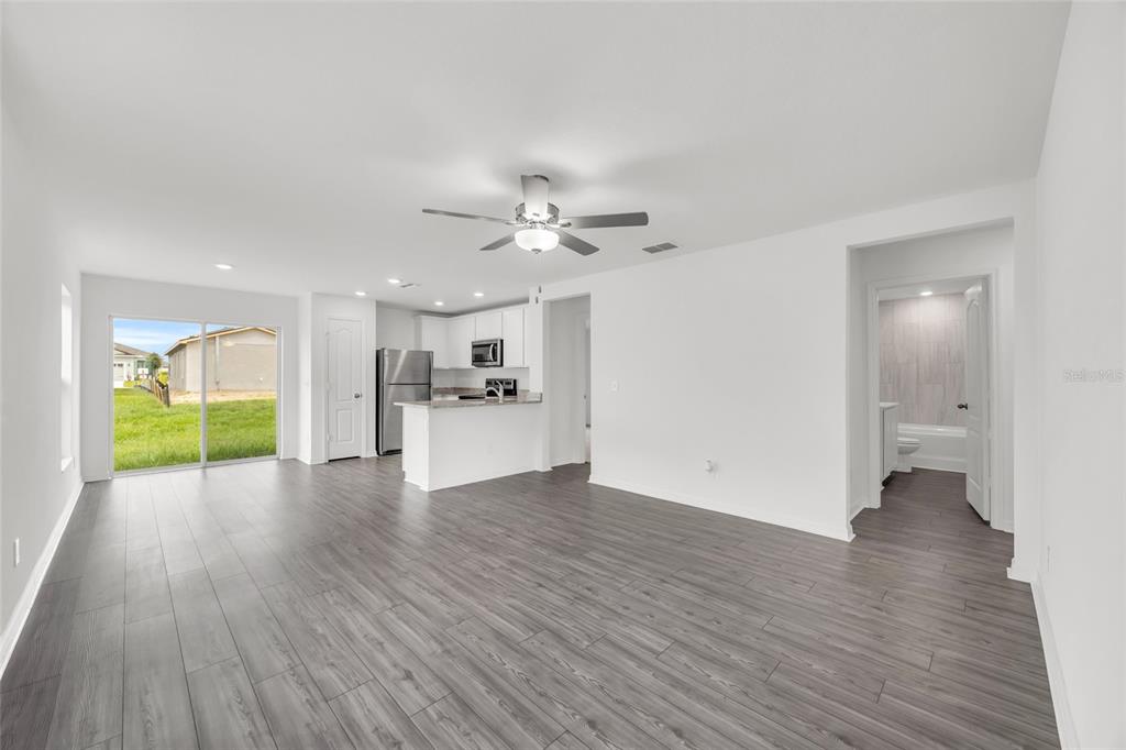 An open-concept living area with gray wood-look flooring, a kitchen, and a sliding glass door — 3824 CORSICAN PLACE, LAKE ALFRED, FL