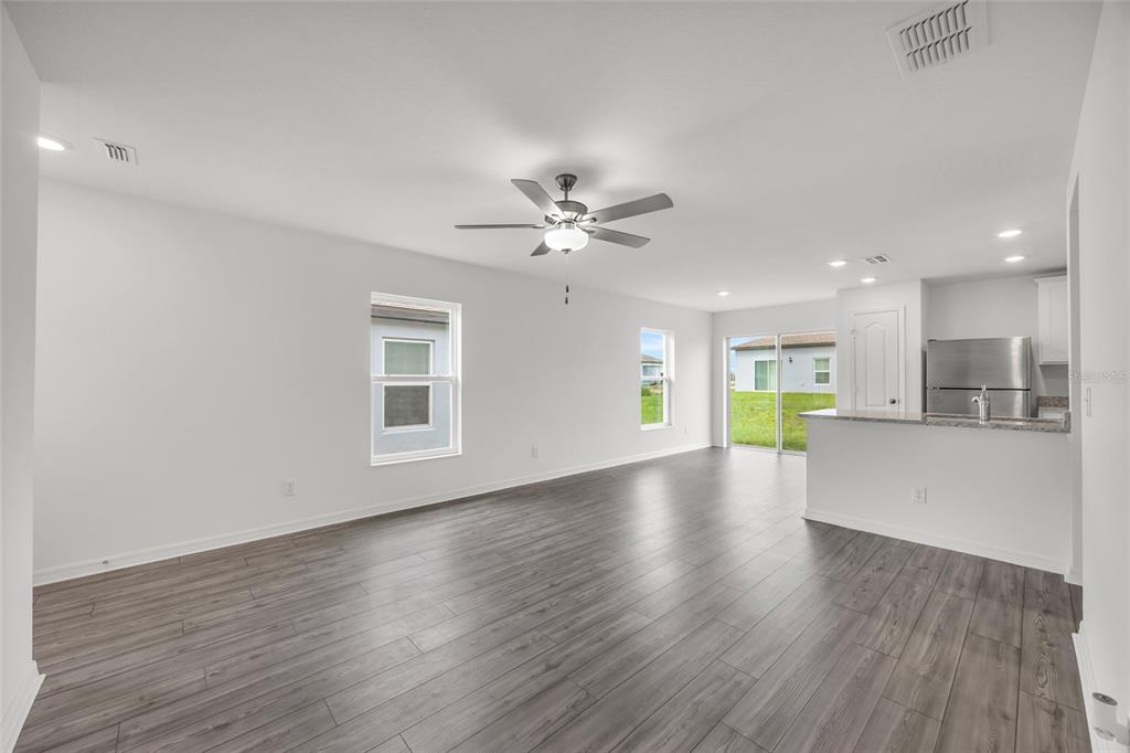 An open-concept living area features gray wood-look flooring, a ceiling fan, and an adjacent kitchen — 3824 CORSICAN PLACE, LAKE ALFRED, FL