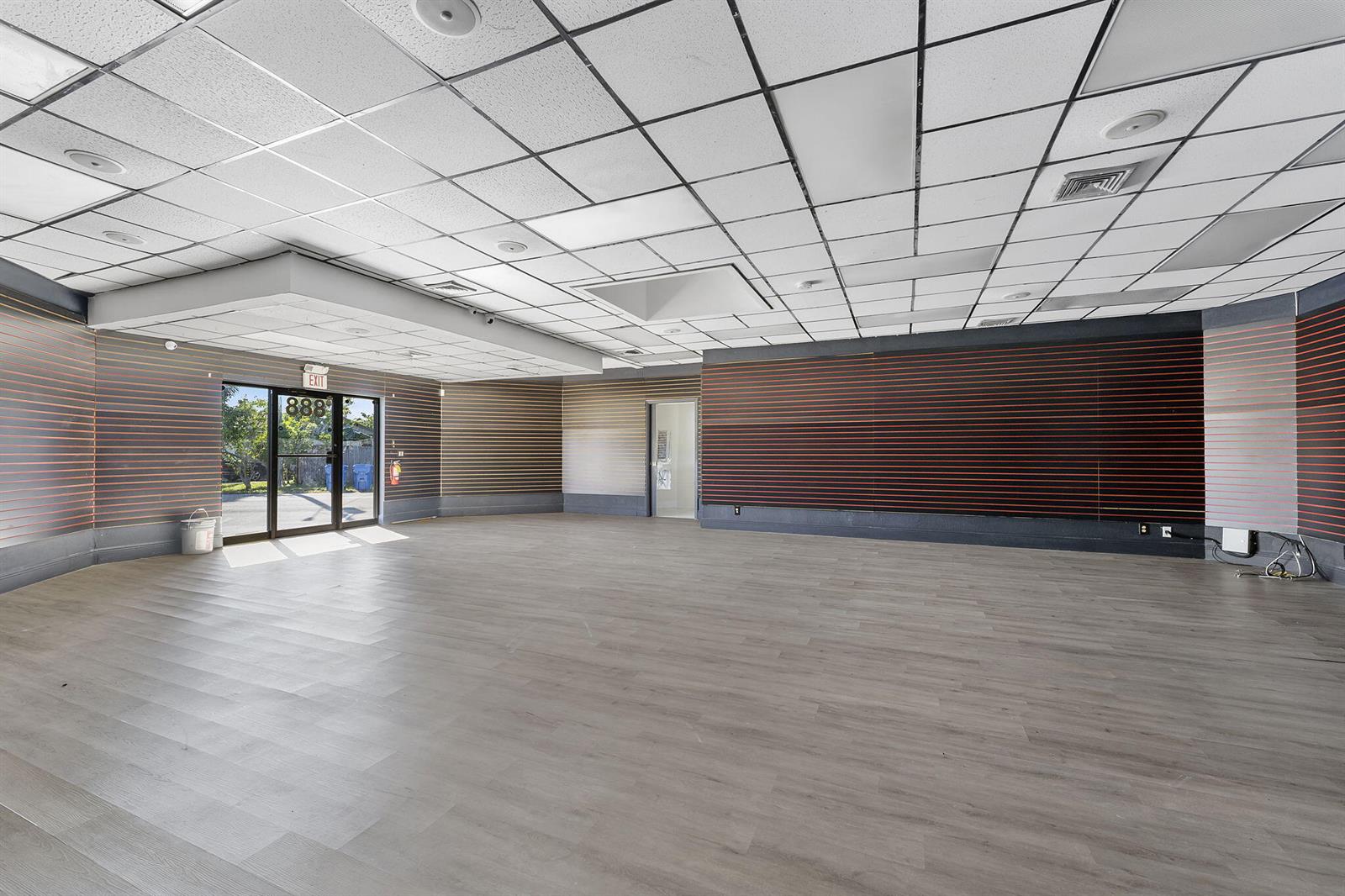 An empty commercial space features wood-look flooring, slat-wall paneling, and a drop ceiling — 888 E Coast Avenue, Lantana FL 33462, LANTANA, FL
