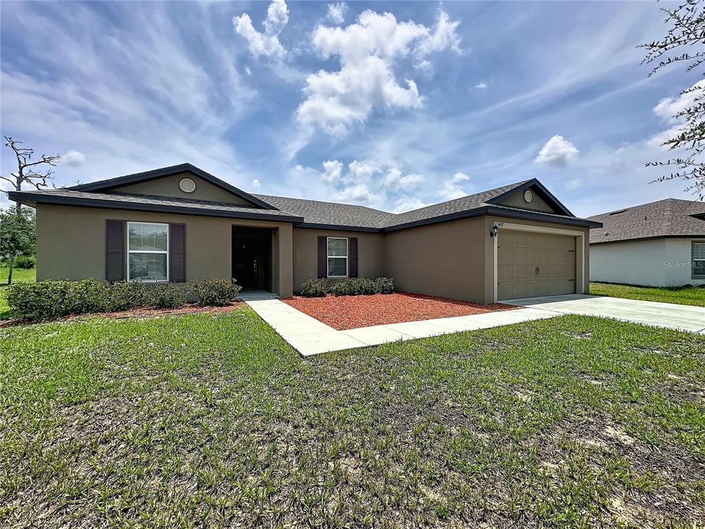 A single-story house with a brown stucco exterior, a two-car garage, and a front lawn — 1407 HILLSBOROUGH WAY, POINCIANA, FL
