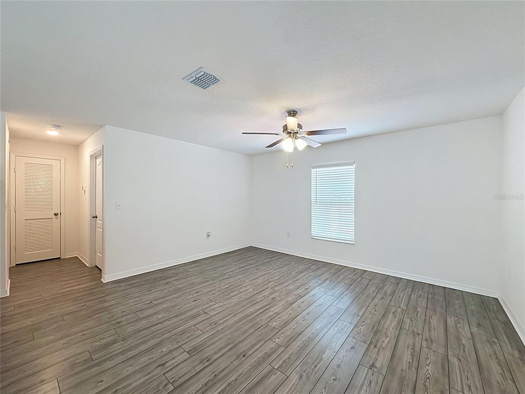 An empty room features white walls, a ceiling fan, and gray wood-look flooring — 1407 HILLSBOROUGH WAY, POINCIANA, FL