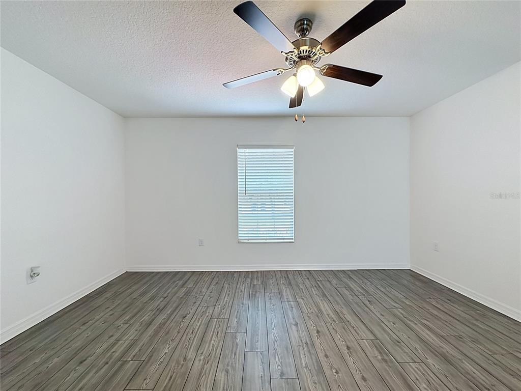 An empty room features white walls, gray wood-look flooring, a window with blinds, and a ceiling fan — 1407 HILLSBOROUGH WAY, POINCIANA, FL