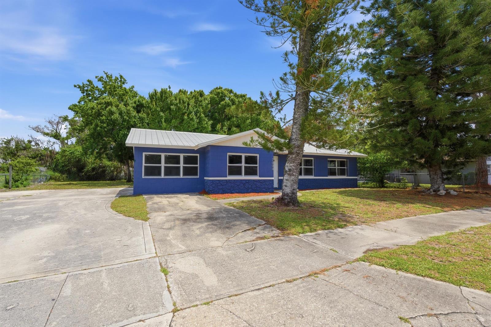 A blue, single-story house with a metal roof and a concrete driveway sits on grass — 3000 Langston Drive, Fort Pierce FL 34946, FORT PIERCE, FL