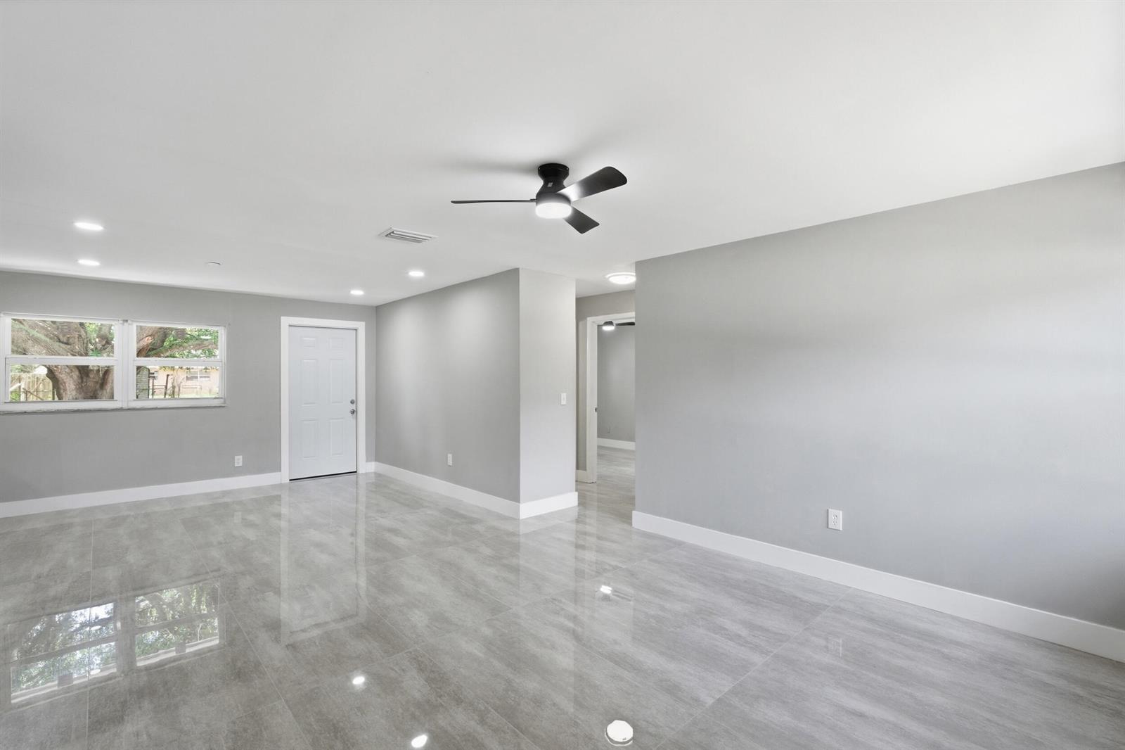 A bright, empty room features gray walls, large glossy floor tiles, and a ceiling fan — 3000 Langston Drive, Fort Pierce FL 34946, FORT PIERCE, FL