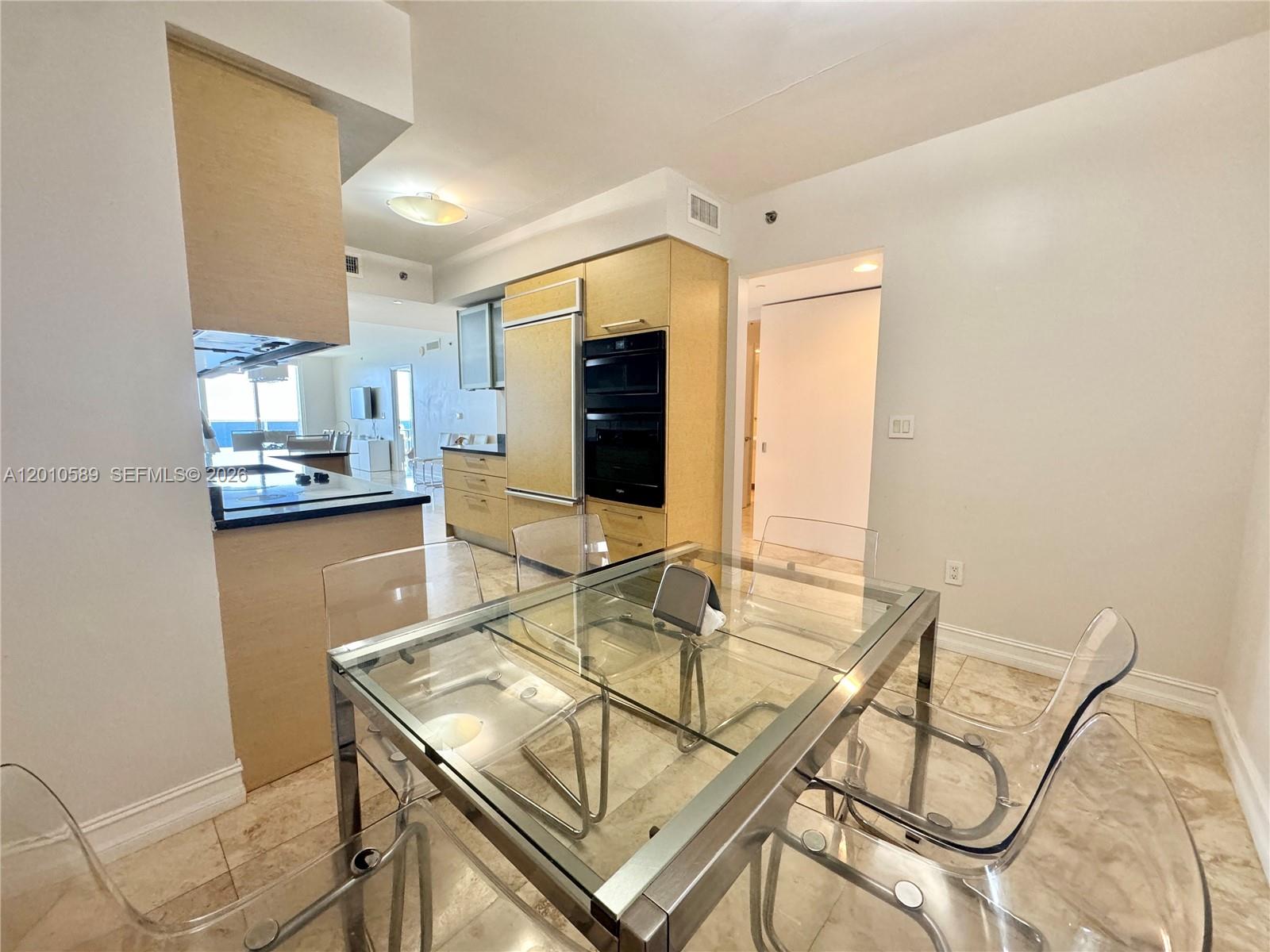 A dining area features a glass table with transparent chairs next to a modern kitchen — 1800 S Ocean Dr # 2602, Hallandale Beach FL 33009, HALLANDALE BEACH, FL