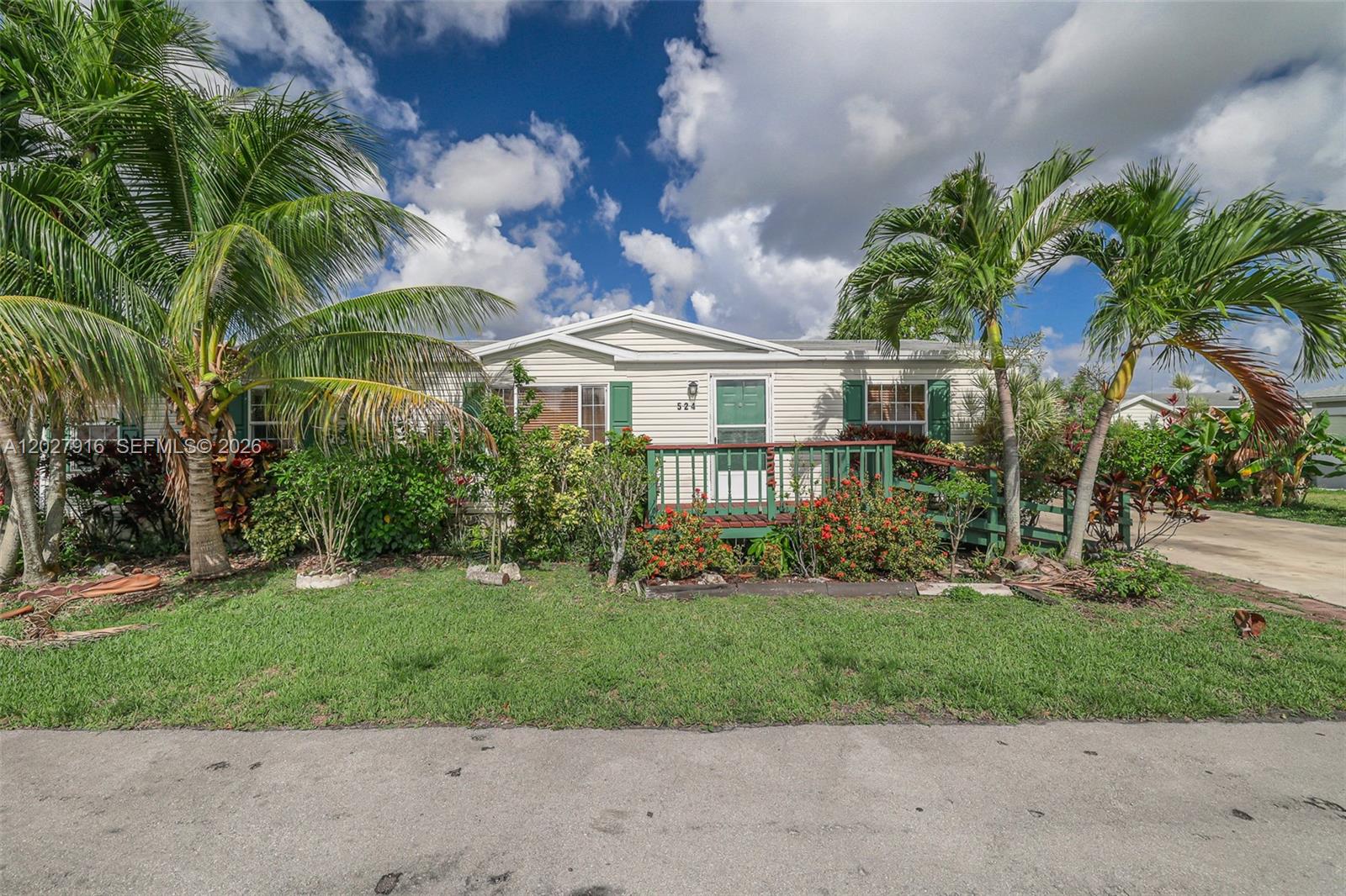 A single-story manufactured home features a green wooden porch, palm trees, and landscaping — 19800 SW 180 avenue #524, Miami FL 33187, MIAMI, FL