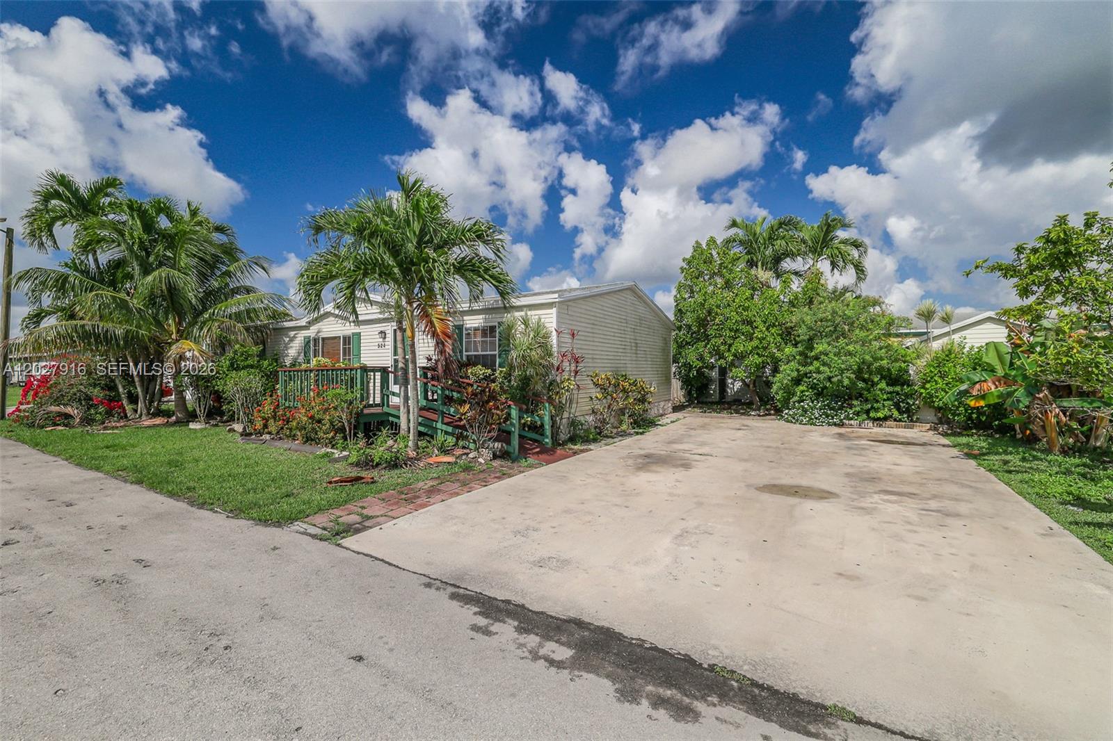 A single-story mobile home features a green wooden deck, a concrete driveway, and palm trees — 19800 SW 180 avenue #524, Miami FL 33187, MIAMI, FL