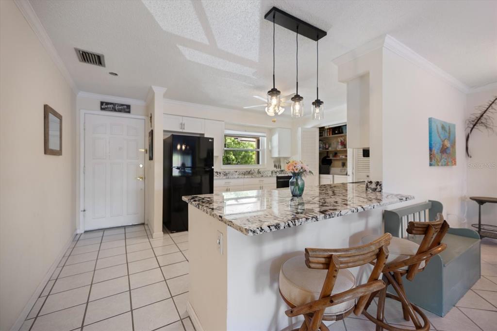 A kitchen with white cabinets, granite countertops, and a breakfast bar opens into a living area — 4522 NARRAGANSET TRAIL UNIT 84, SARASOTA, FL