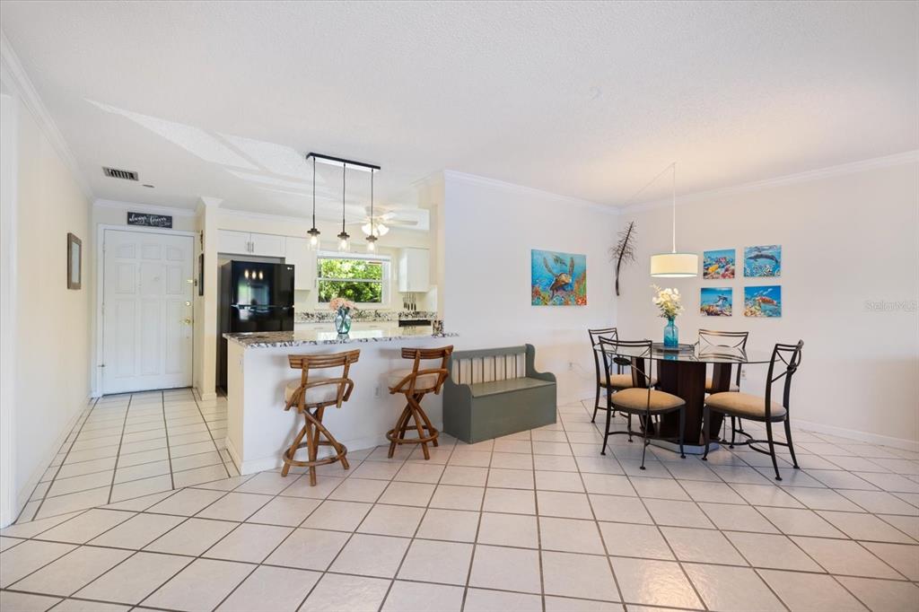 A kitchen features a granite-topped island, black refrigerator, white cabinets, and three pendant lights — 4522 NARRAGANSET TRAIL UNIT 84, SARASOTA, FL