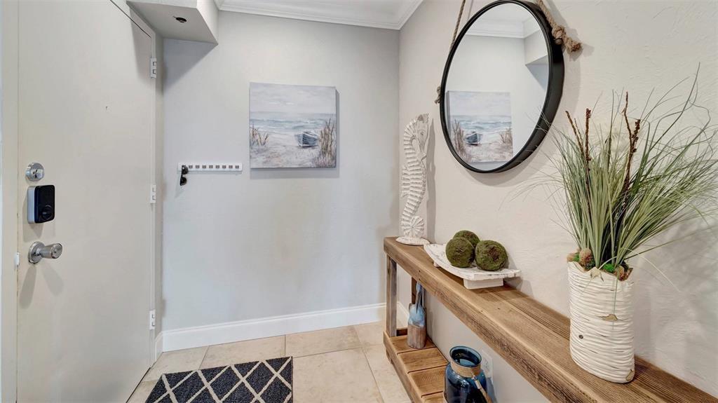 An entryway features a wooden console table, a round mirror, and coastal-themed wall art — 1125 W PEPPERTREE DRIVE UNIT 705, SARASOTA, FL