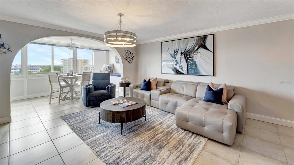 A living room with a gray sectional, blue armchair, round coffee table, and arched window area — 1125 W PEPPERTREE DRIVE UNIT 705, SARASOTA, FL