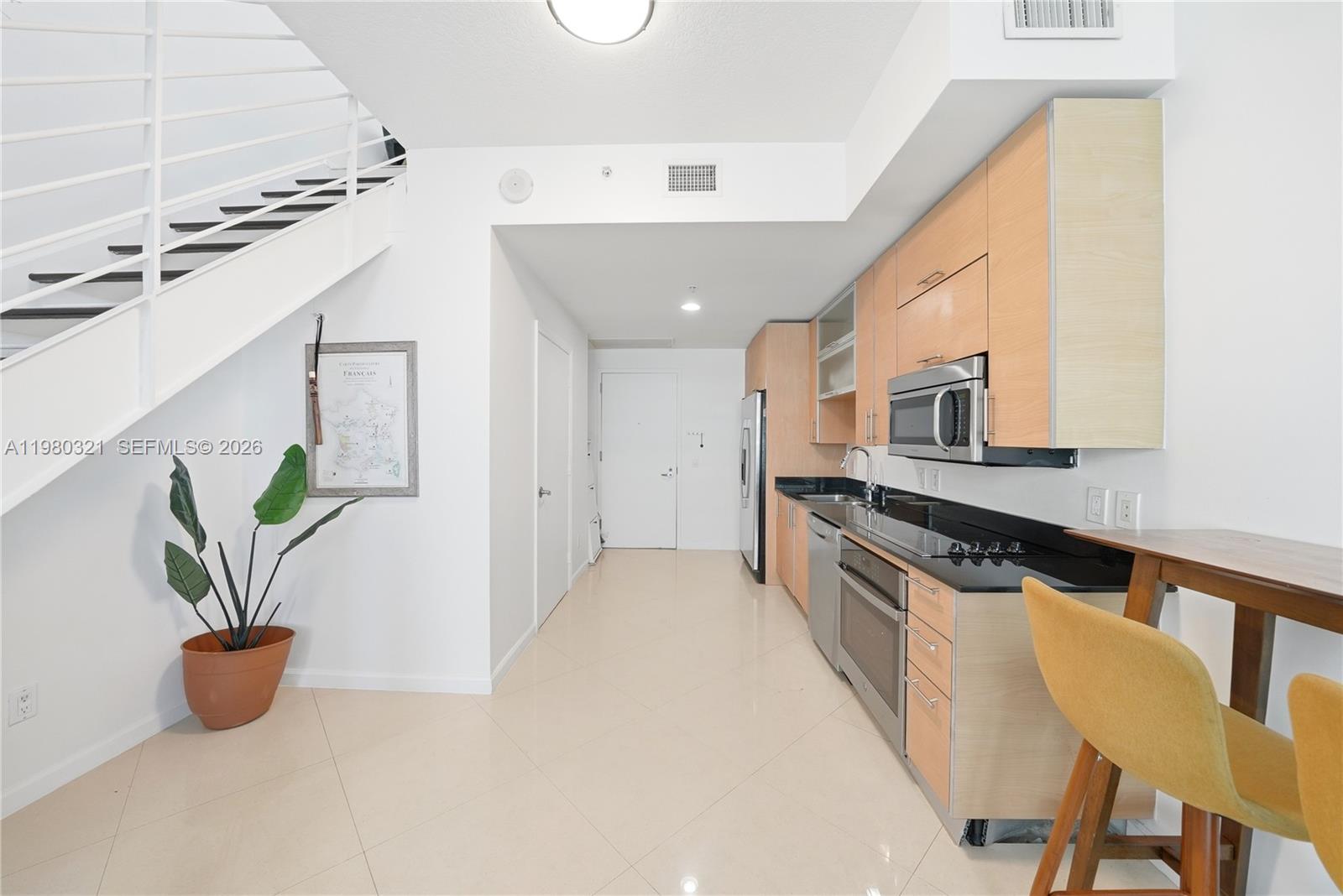 A kitchen with light wood cabinets, black countertops, and a staircase on the left — 60 SW 13th St # 4414, Miami FL 33130, MIAMI, FL
