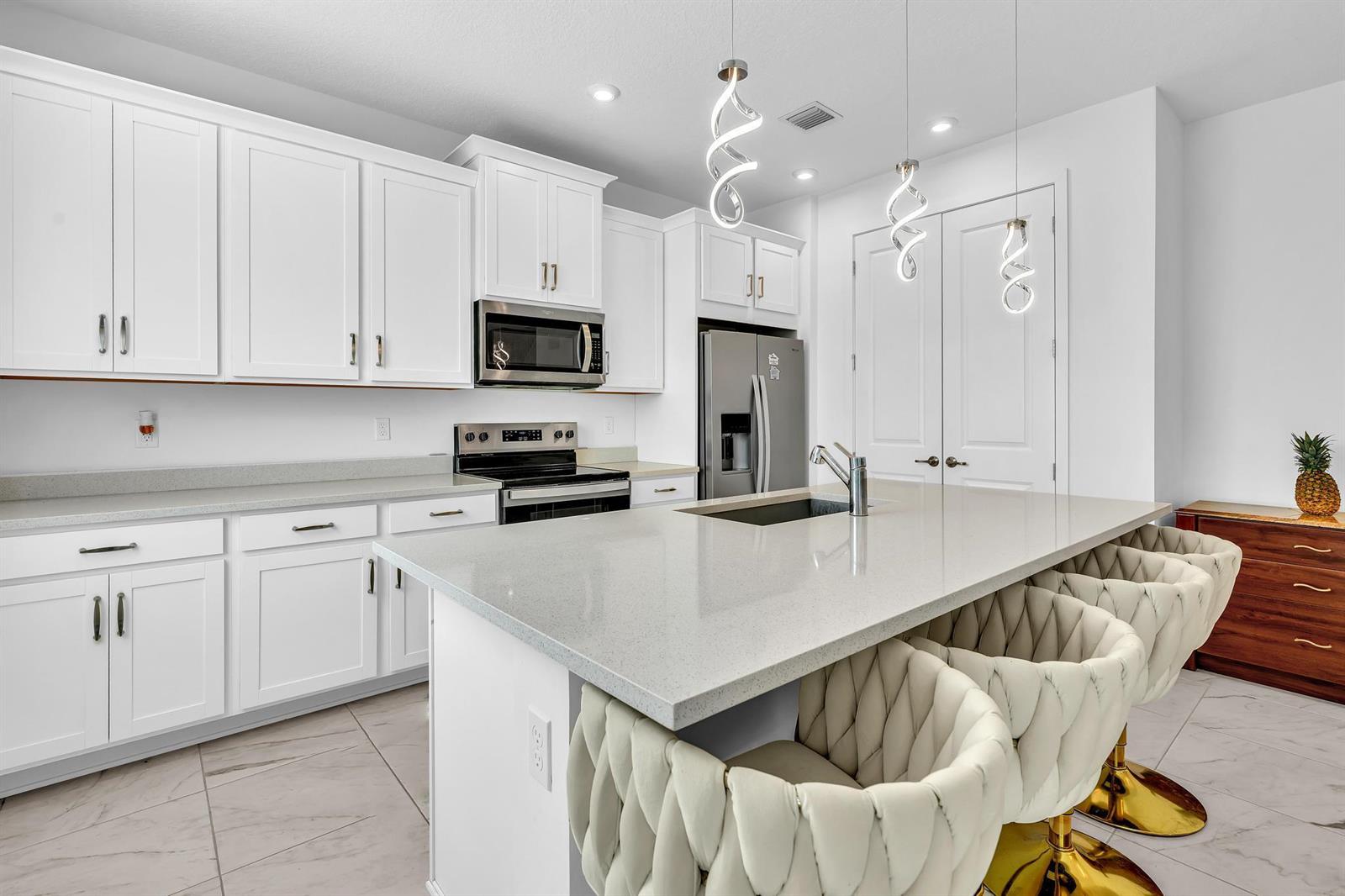 A modern kitchen features white cabinets, quartz countertops, a central island, and three bar stools — 7268 Lenora Lane, Lake Worth FL 33467, LAKE WORTH, FL