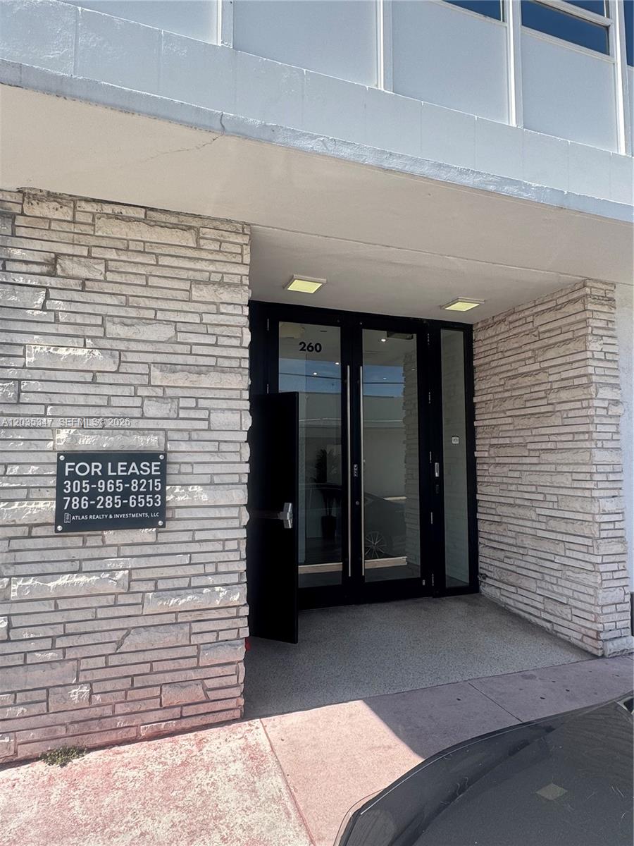 The exterior entrance of a commercial building features a stone facade and glass double doors — 9491 Harding Ave # 205, Surfside FL 33154, SURFSIDE, FL