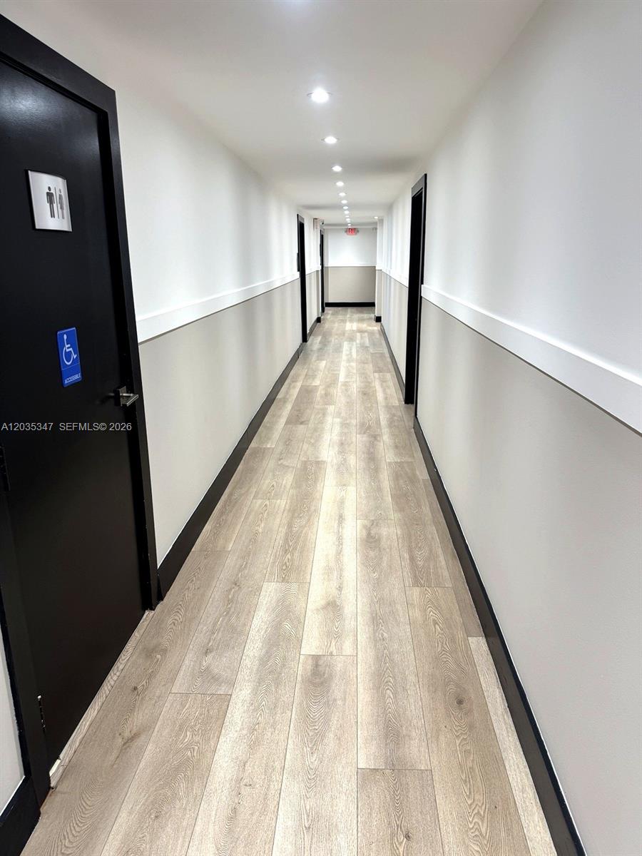 A long hallway features light wood-look flooring, white walls with gray wainscoting, and black doors — 9491 Harding Ave # 205, Surfside FL 33154, SURFSIDE, FL